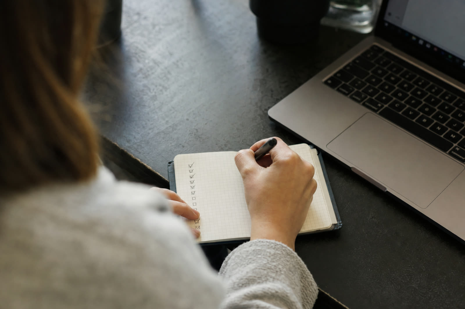 Handen vinken punten af op een checklist naast een laptop